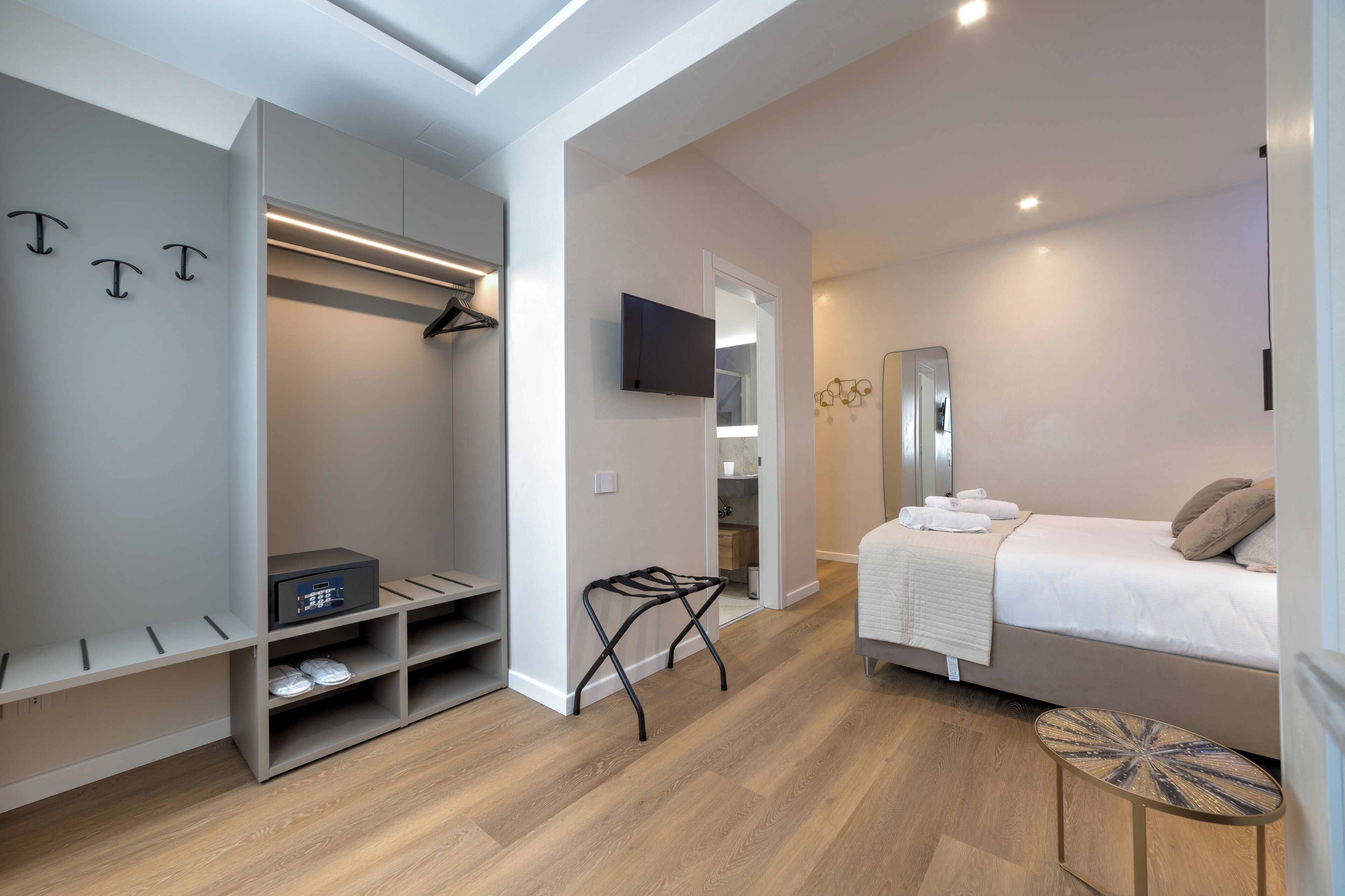Ein modernes Hotelzimmer mit Bett, Fernseher, begehbarem Kleiderschrank und einem kleinen Tisch.