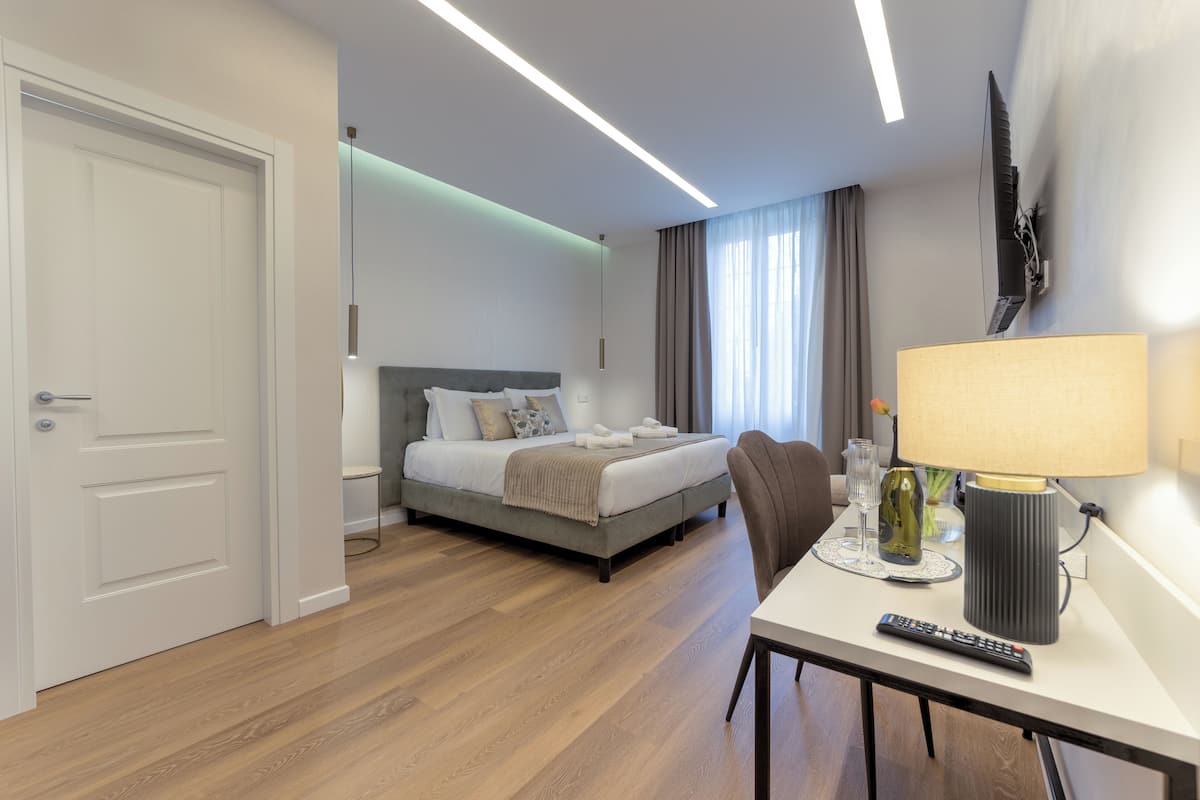 A modern hotel room with a bed, bedside table, lamp, and a TV mounted on the wall.