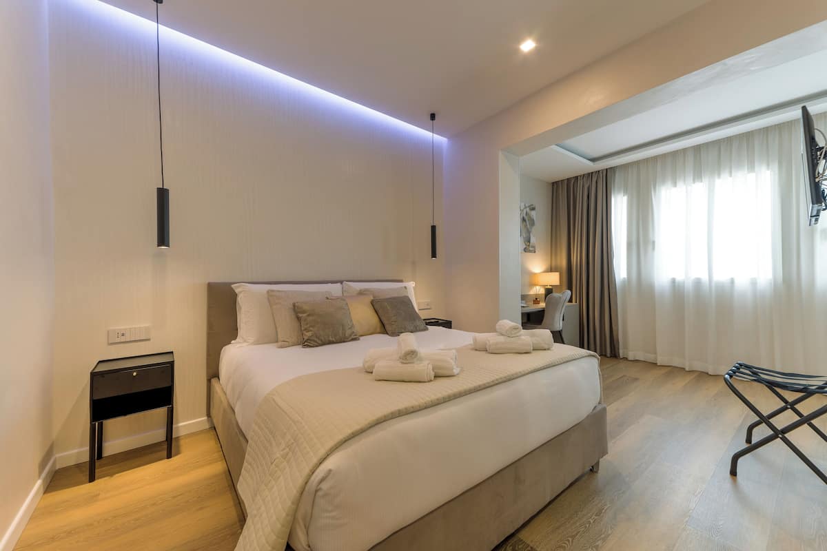 A modern hotel room with a large bed, bedside tables, a flat-screen TV, and a view of the outdoors.