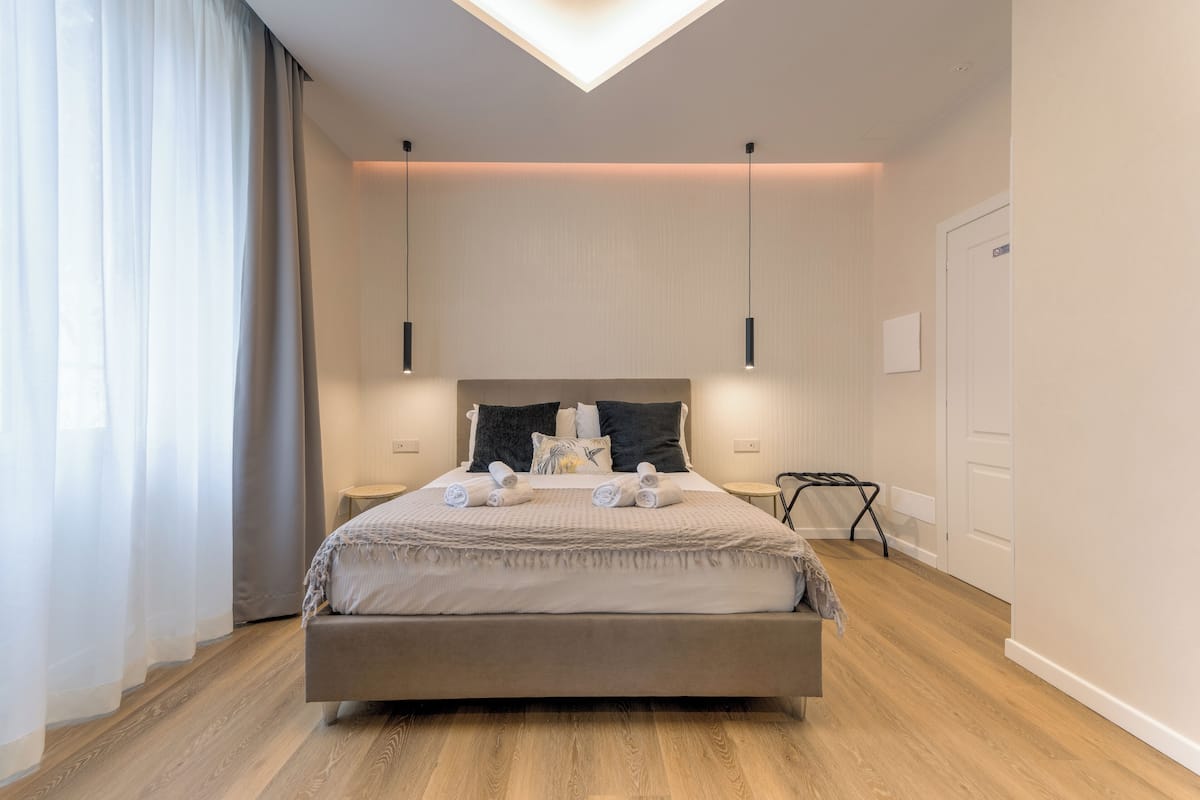 A modern bedroom with a large bed, bedside tables, a ceiling light, and a door.