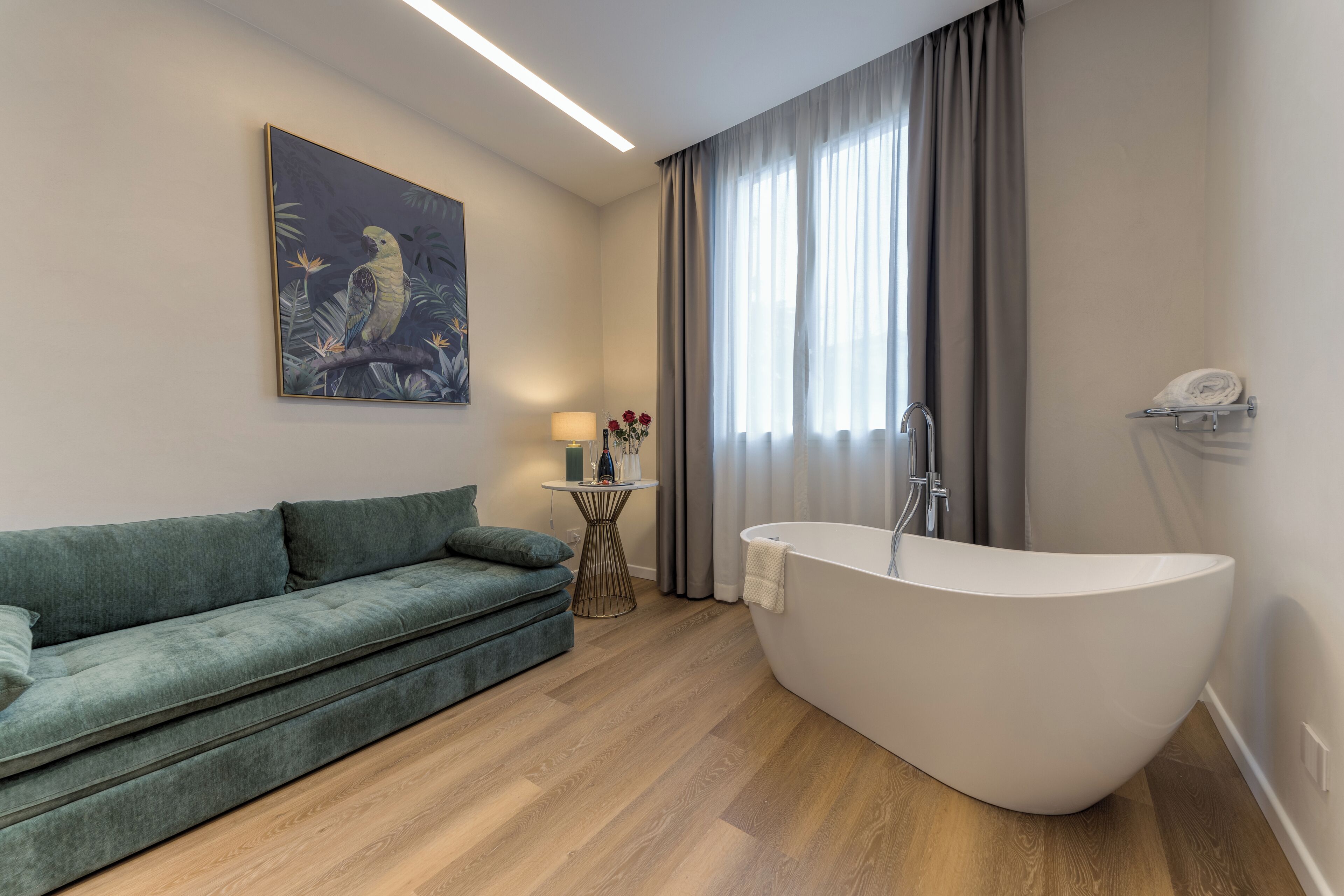 A modern bathroom with a freestanding bathtub, a green sofa, a small table with a lamp, and a painting on the wall.