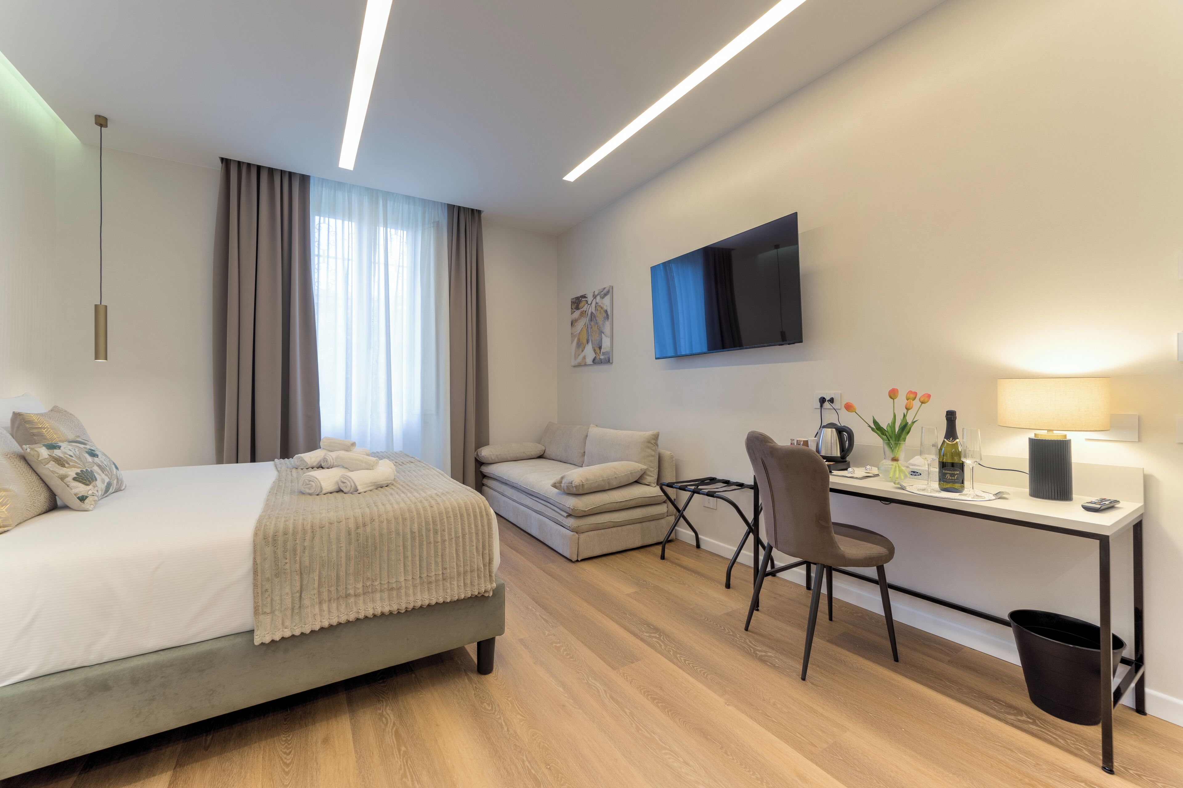 Ein modernes Hotelzimmer mit einem Bett, einem Schreibtisch, einem Sessel, einer Couch und einem Fernseher.