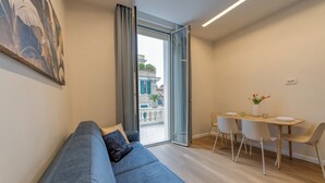 A modern living room with a blue sofa, a dining table with chairs, and a large window with a view of buildings. - GH Villa Poerio (Rome)