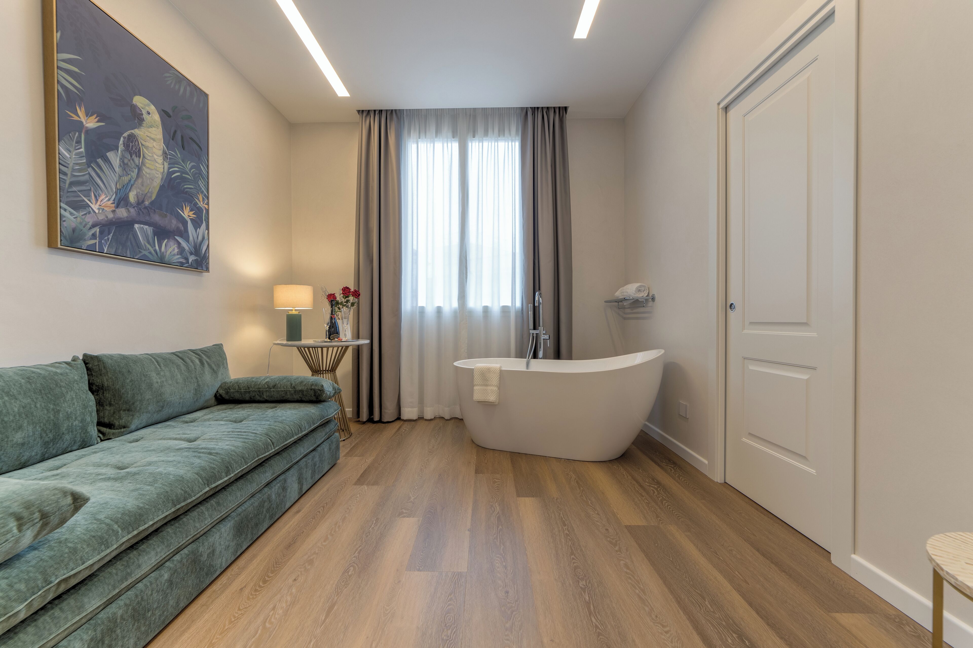 A modern bathroom with a freestanding bathtub, a sofa, and a painting on the wall.
