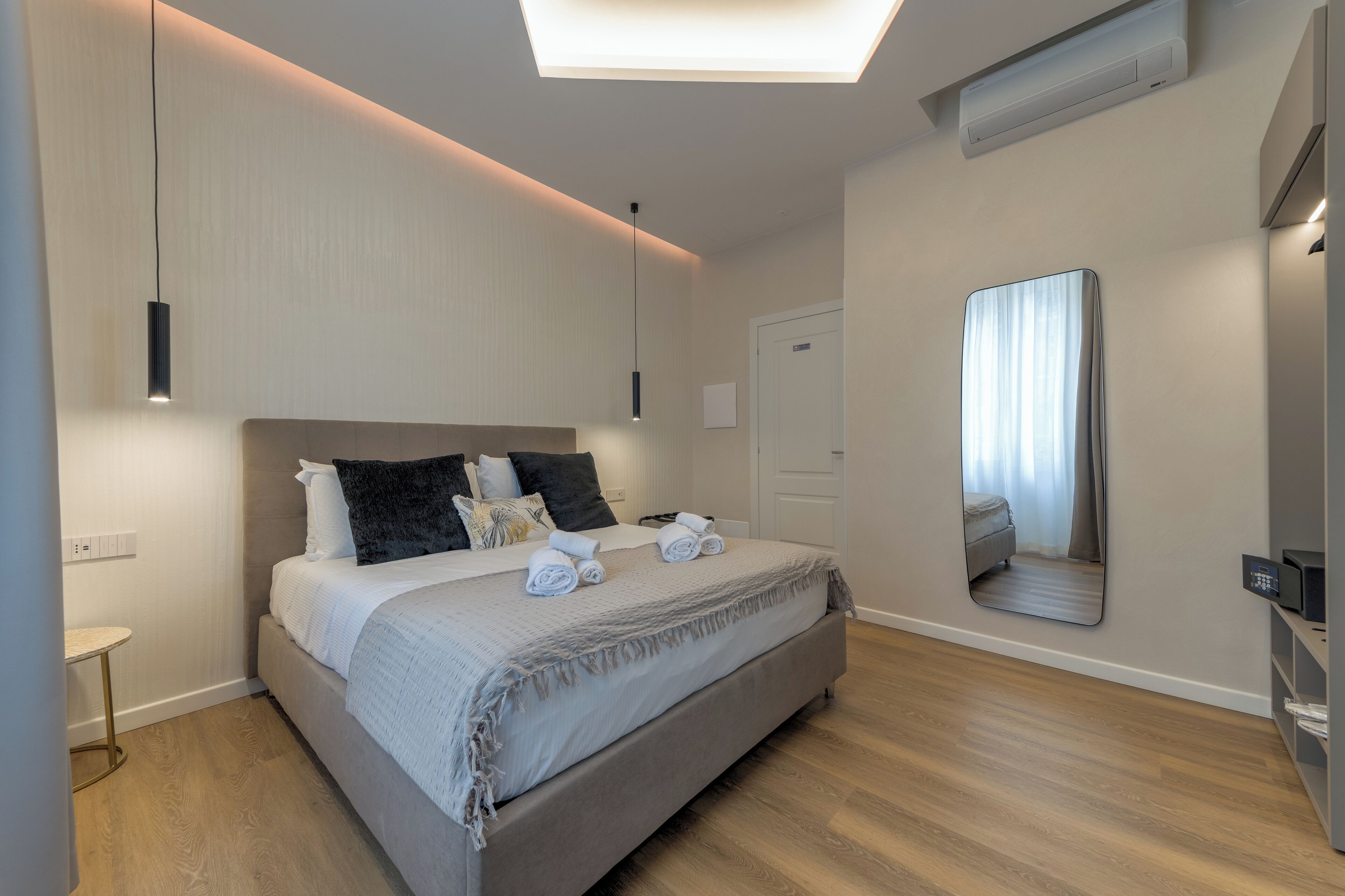 A modern bedroom with a large bed, bedside tables, a mirror, and a ceiling light.