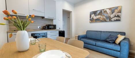 A modern kitchen with white cabinets, a dining table set with plates and cutlery, a blue sofa, and a wall-mounted painting.