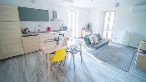 Een moderne keuken met houten kasten, een eettafel met gele stoelen, een grijze bank en een grijs vloerkleed.