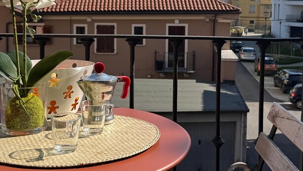 Een balkon met een tafel, een potorkidee, een theepot en een karaf. Achtergrond: een gebouw met een koepel en een pannendak.