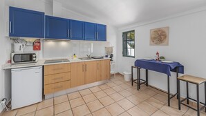 A compact kitchen with blue cabinets, a microwave, a small refrigerator, and a dining area with a table and chairs. - Jardim do Sul Apt 6 (Olhao)