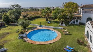 A circular swimming pool with a surrounding deck, a lawn, and a view of a coastal town. - Jardim do Sul Apt 6 (Olhao)