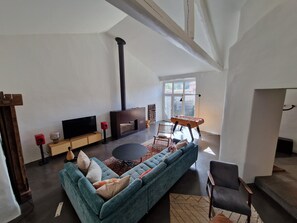 Ein geräumiges Wohnzimmer mit einer großen Couch, einem Kamin, einem Fernseher und einem Fenster mit Blick ins Freie.