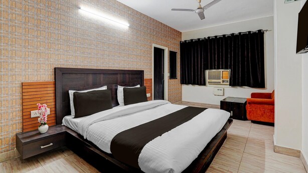 A hotel room with a large bed, a nightstand, a small table, a chair, a ceiling fan, and a window with curtains. - Hotel O Clock Tower Ludhiana (Ludhiana)