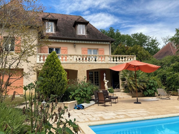A two-story house with a balcony, a swimming pool, and outdoor furniture.