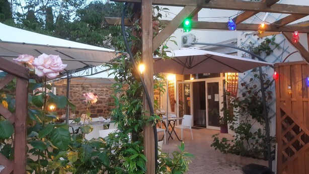 A covered outdoor seating area with tables and chairs, surrounded by greenery and a wooden pergola structure. - Auberge de la Couronne (Lablachère)