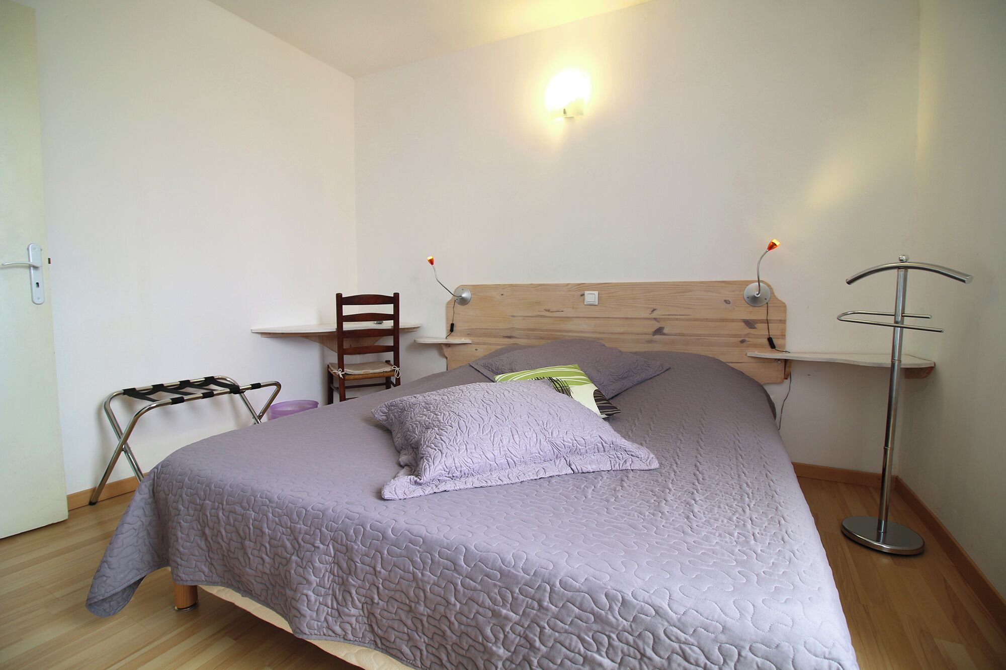 Ein Schlafzimmer mit einem Bett, einem hölzernen Kopfende, einem Sessel, einem Schreibtisch und einer Stehlampe.