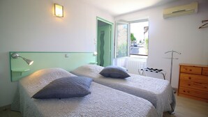 A room with two beds, a wooden dresser, a radiator, and a window with a view of the street. - Auberge de la Couronne (Lablachère)