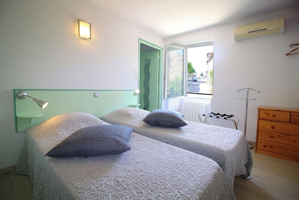 A room with two beds, a wooden dresser, a radiator, and a window with a view of the street. - Auberge de la Couronne (Lablachère)
