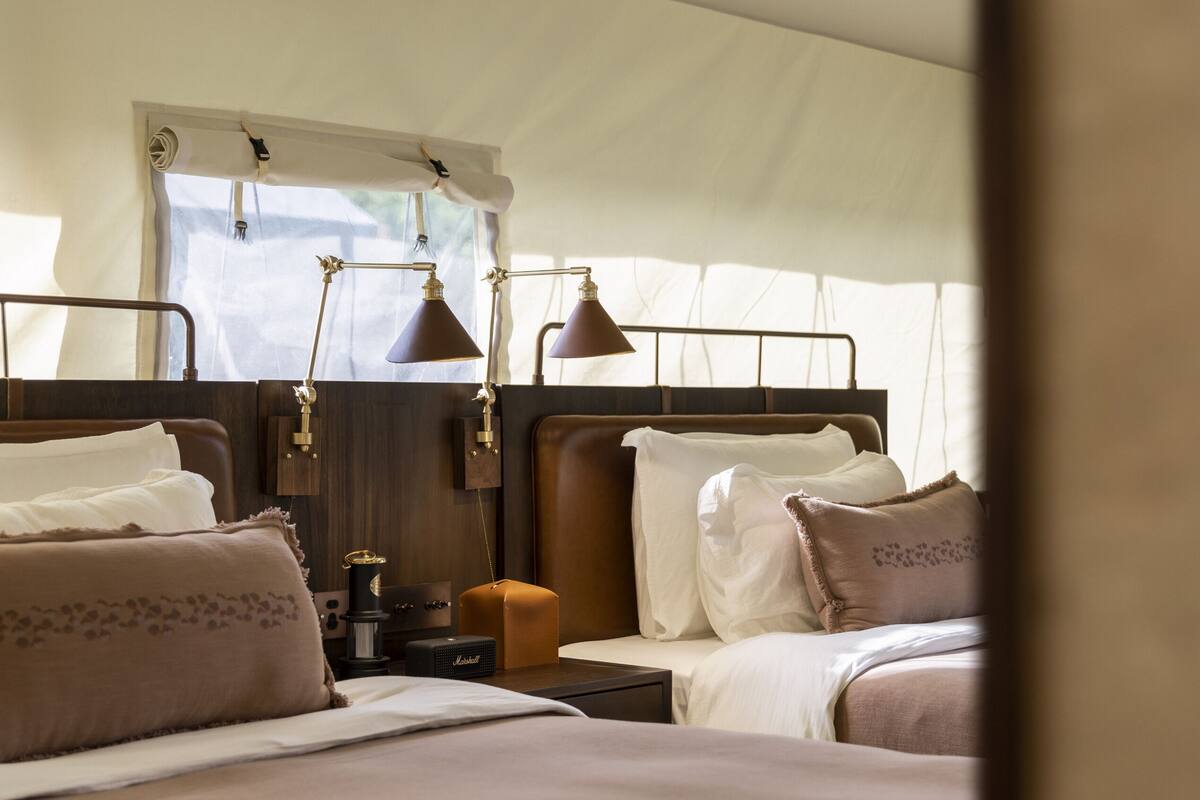 A tented accommodation with two beds, each with a lamp, a small table, and a radio.