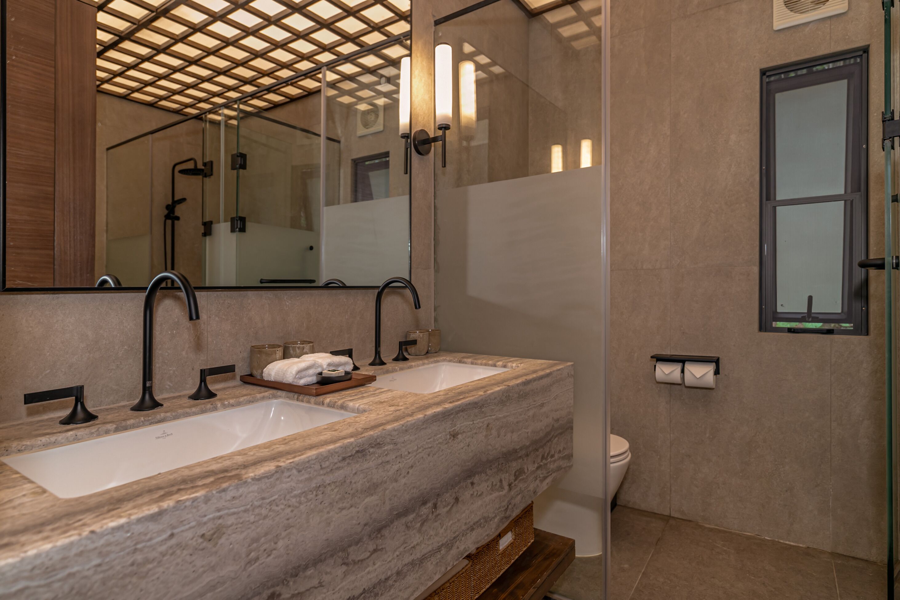 A bathroom with a large mirror, two sinks, a shower, and a toilet.