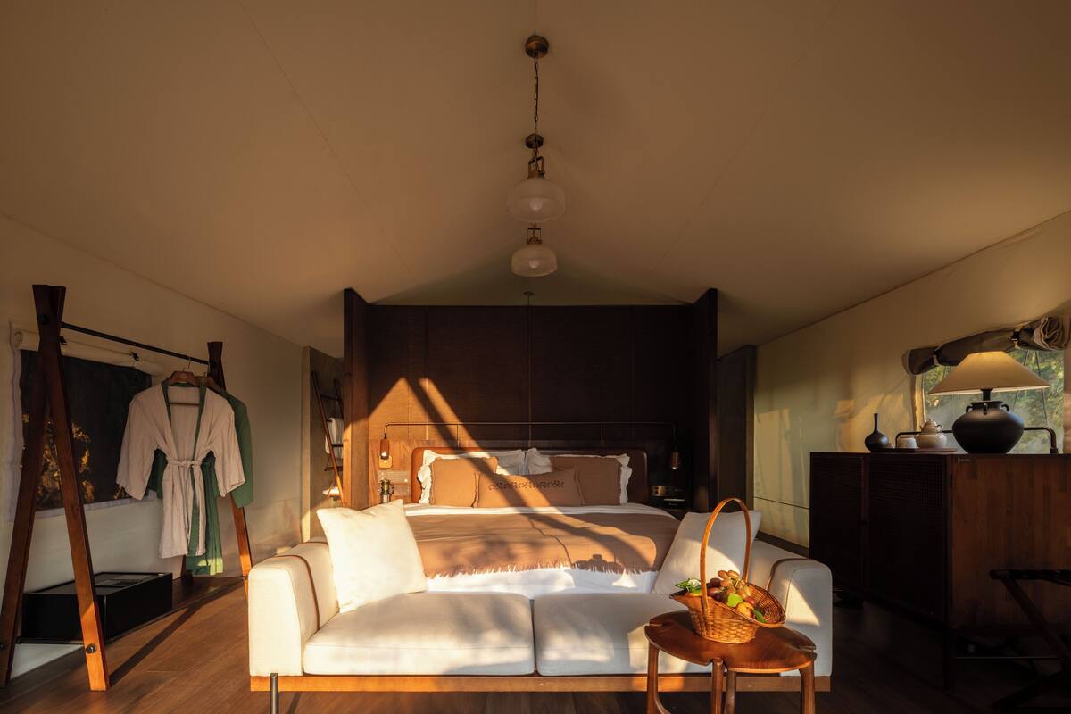 A bedroom with a bed, a bedside table with a lamp, a wooden dresser, and a window.