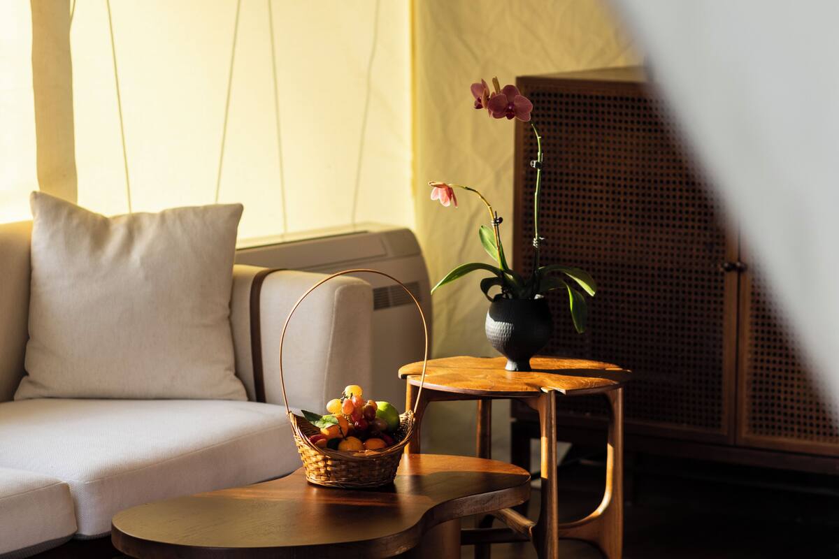 A room with a sofa, a small wooden table, a wicker basket with fruit, and a potted orchid.