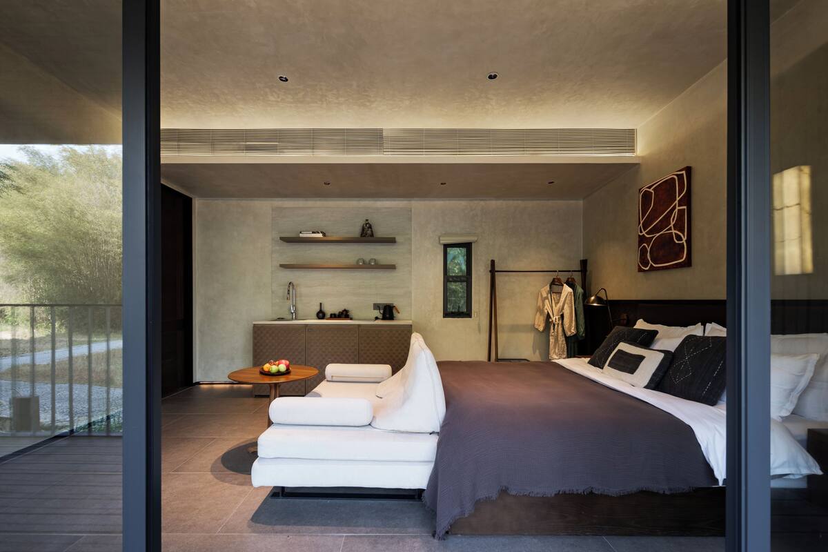 A modern bedroom with a large bed, a sofa, a small table, and a kitchenette area.
