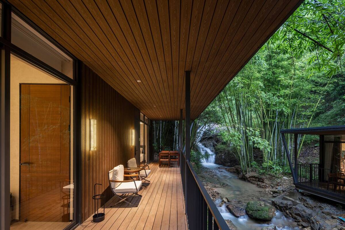 A wooden deck with outdoor seating, a view of a bamboo forest, and a stream.
