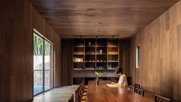A modern dining room with a long wooden table, chairs, and a bookshelf filled with books and decorative items.
