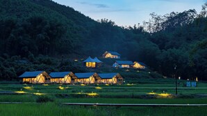 A cluster of rustic cabins with sloped roofs, surrounded by lush greenery and hills. - SINYE IN THE VALLEY (Guangzhou)