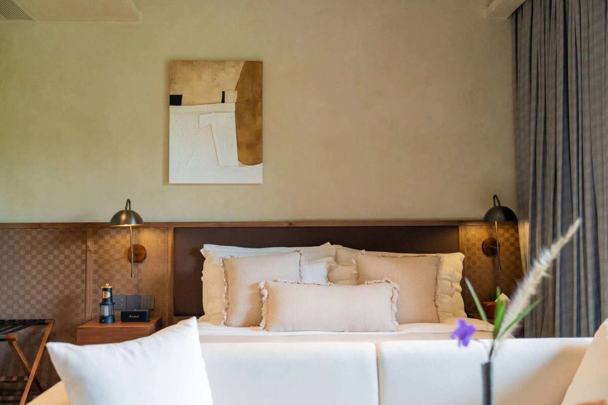 A hotel room with a bed, bedside lamps, a nightstand, and a wall-mounted artwork.