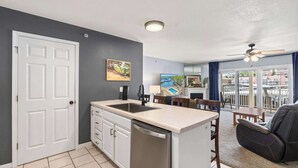A compact kitchen with a dishwasher, a dining area with a table and chairs, and a balcony with a view of the city. - Lake Mode Lakefront Balcony (Osage Beach)
