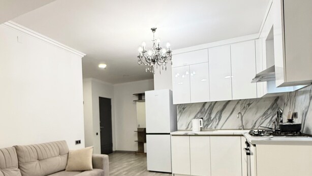 Ein modernes Wohnzimmer mit einer Couch, einem Marmortisch und einer Küche mit weißen Schränken und einer Marmor-Spritzschutzwand.