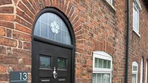 Un edificio de ladrillo con una puerta negra, una placa con el número 13 y una ventana con contraventanas.