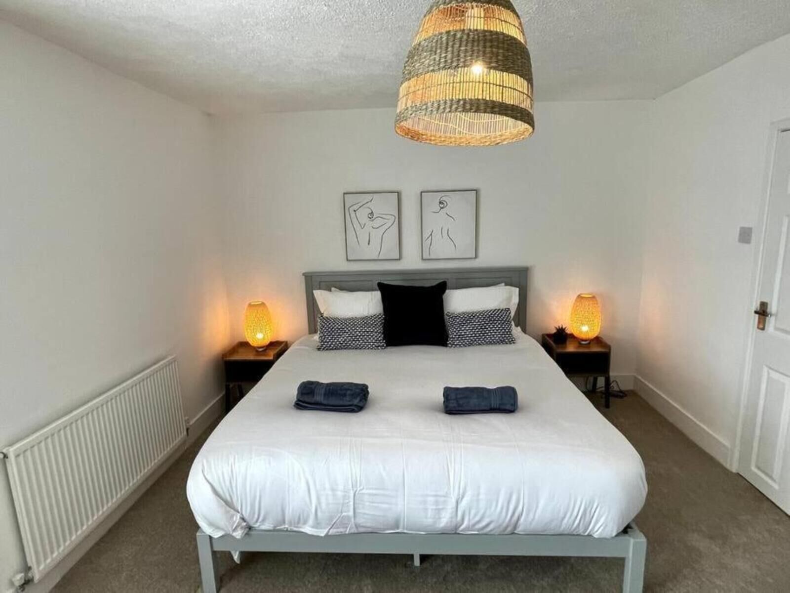 A bedroom with a bed, two bedside lamps, a hanging light fixture, and two wall art pieces.