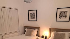 Una habitación de hotel con dos camas individuales, una mesita de noche con lámpara y cuadros en las paredes.
