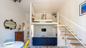 Ein Schlafzimmer im Loft-Stil mit Etagenbett, einem Essbereich mit Tisch und Stühlen, einer Treppe und einem an der Wand montierten Fernseher.