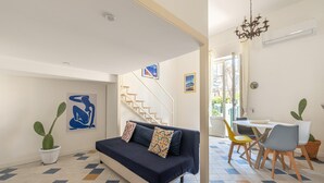Ein Wohnzimmer mit einer Couch, einem Esstisch mit Stühlen, einer Treppe und einem Chandelier.