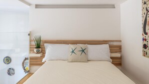 Ein Schlafzimmer mit einem hölzernen Kopfteil, zwei mit Sternenmuster versehenen Kissen, einem Blumentopf und dekorativen Tellern an der Wand.