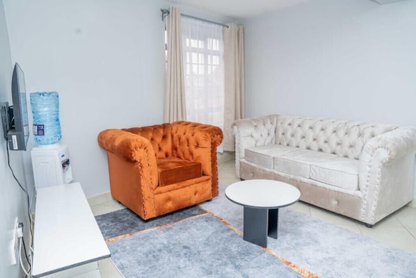 A room with a white sofa, an orange armchair, a small white table, and a water dispenser.