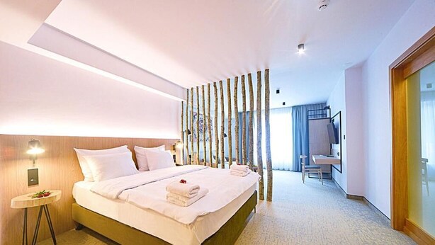 Una camera d'hotel con un letto grande, un comodino, una scrivania con una sedia, uno specchio e una porta scorrevole.