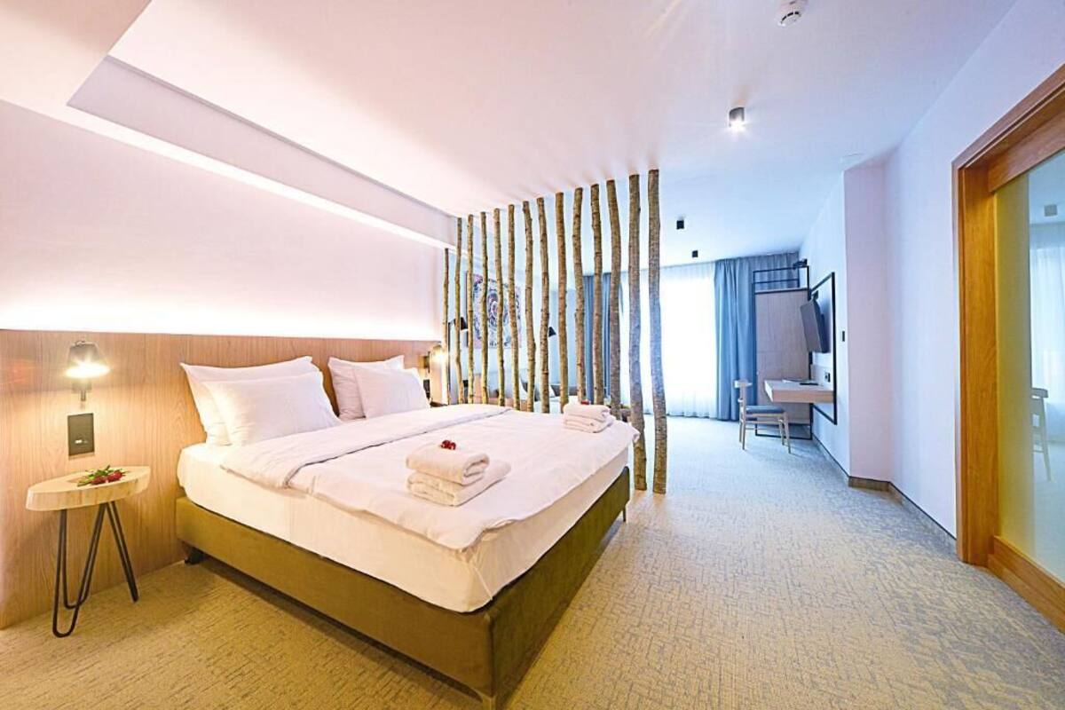 A hotel room with a large bed, a small bedside table, a desk with a chair, a mirror, and a sliding door.