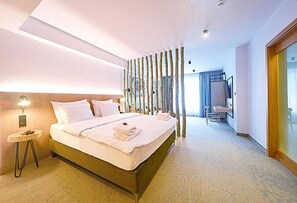 A hotel room with a large bed, a small bedside table, a desk with a chair, a mirror, and a sliding door.