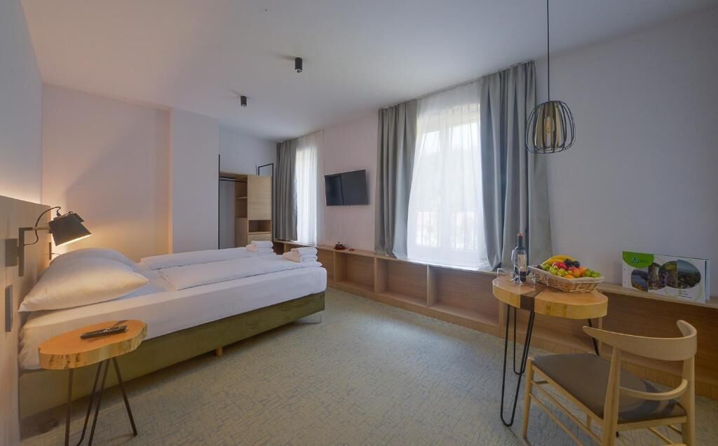 A hotel room with a bed, a desk, a chair, a TV, and a window with curtains.