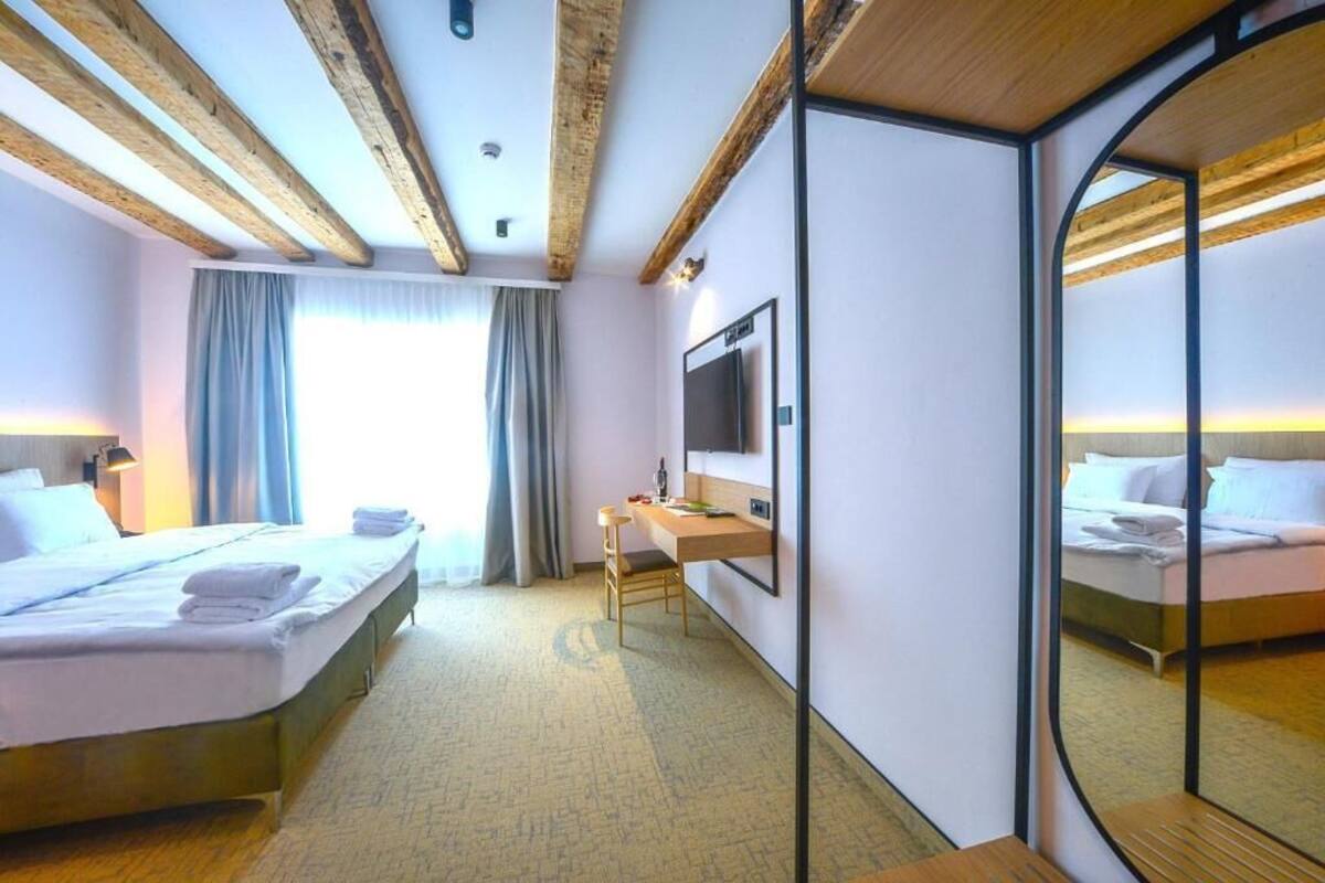 A hotel room with a bed, a desk, a chair, a TV, and a large mirror.