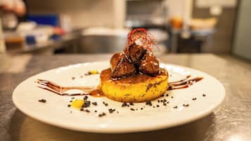 Un dessert servi dans une assiette blanche, avec une couche de caramel sur le dessus, décoré d’un fin ruban rouge et de copeaux de chocolat.