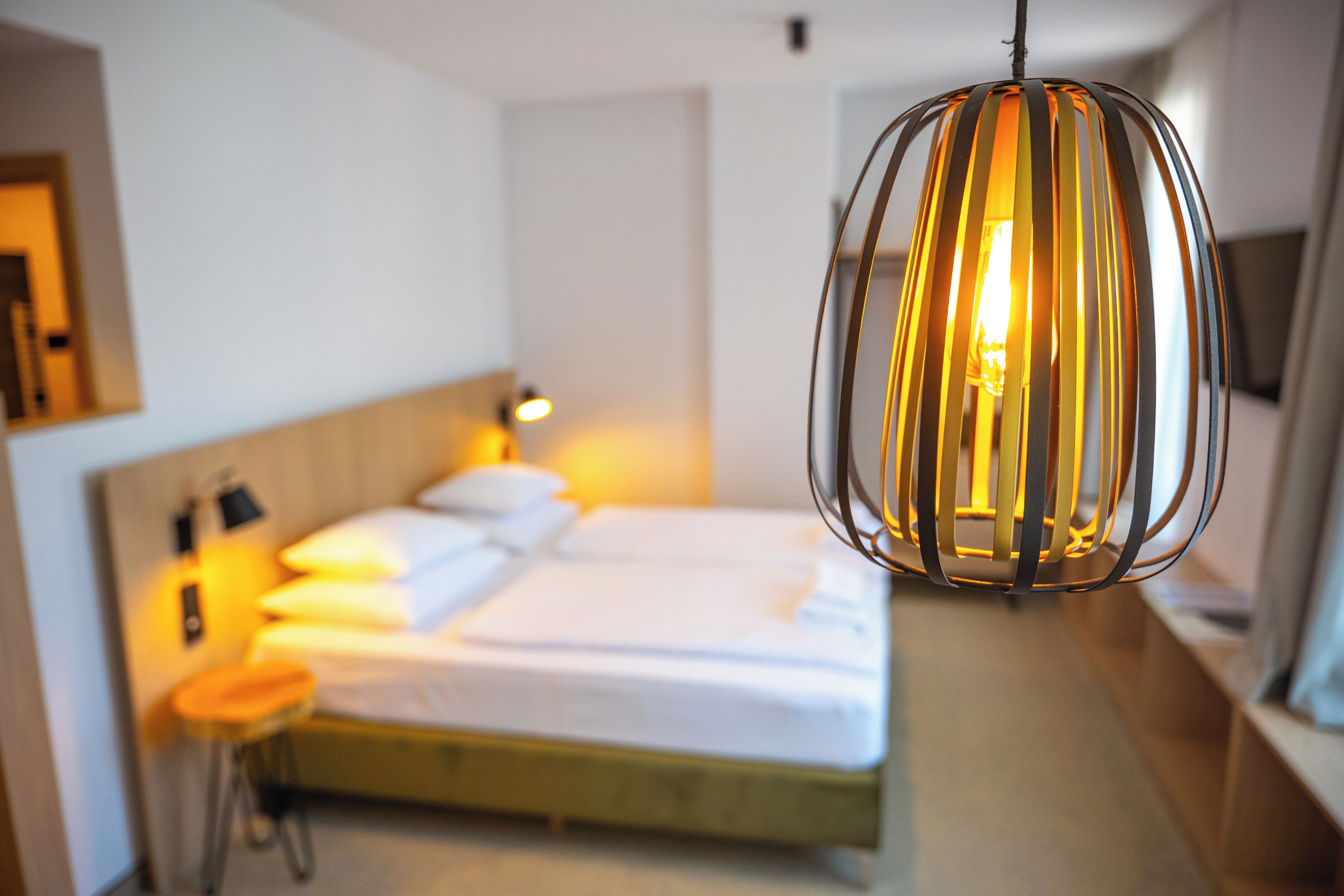 Une chambre d’hôtel avec un lit, une table de chevet, une lampe et un luminaire suspendu.