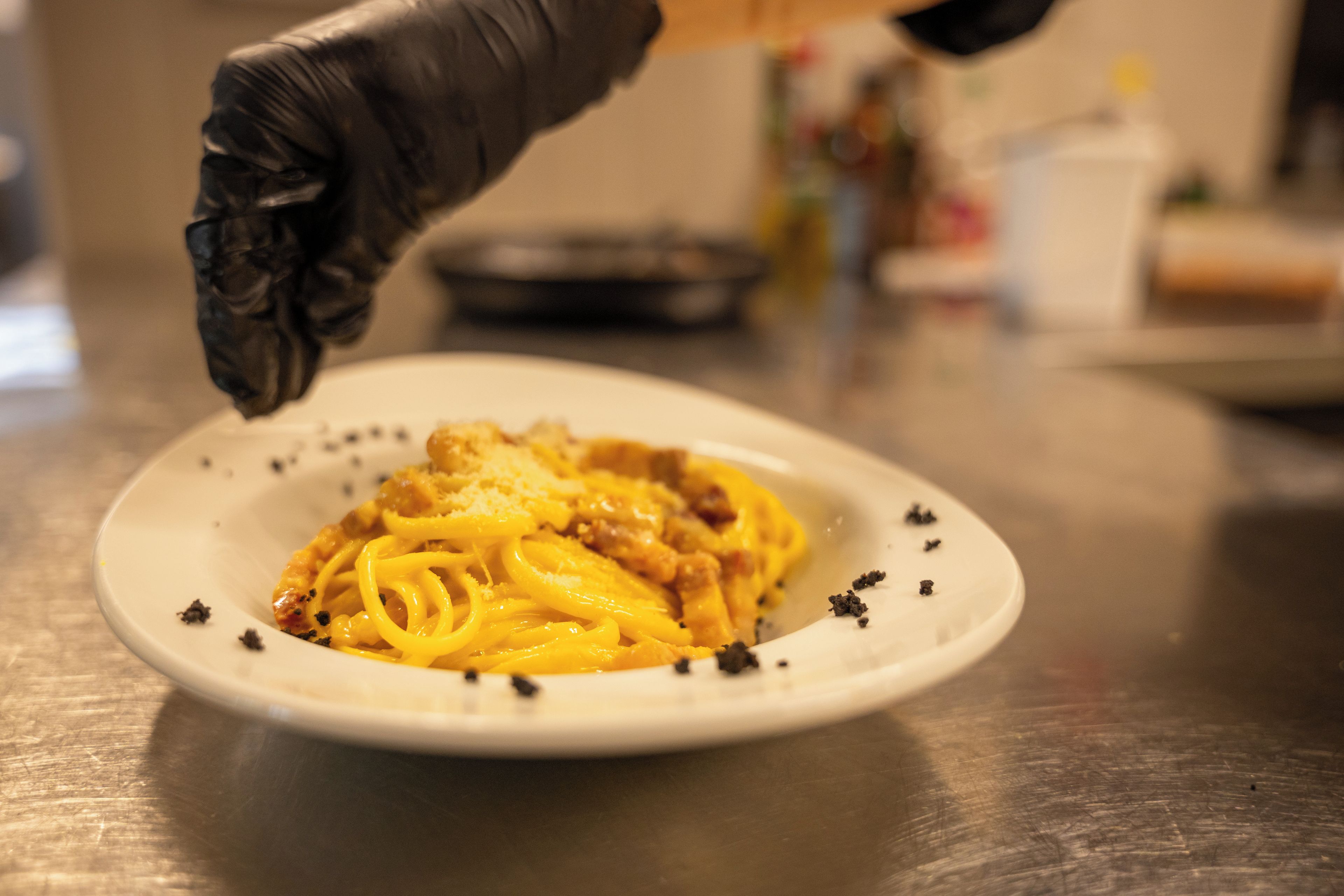 Un plato de espagueti con salsa cremosa y queso rallado, adornado con pimienta negra, sobre una mesa de madera.