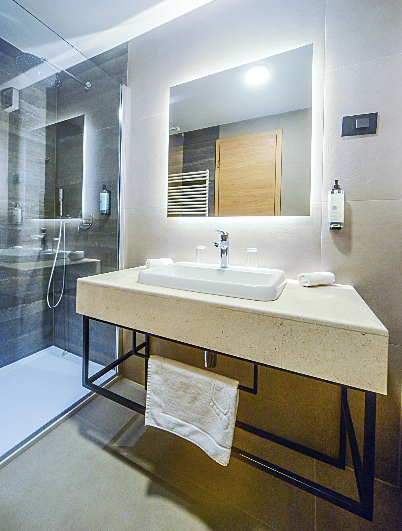 Une salle de bain moderne avec une douche à parois de verre, un grand miroir et un plan de toilette doté d’un lavabo et d’un porte-serviettes.