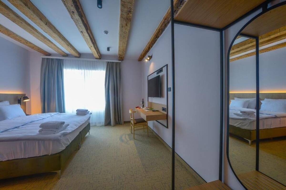 A hotel room with a bed, a desk, a mirror, and a TV.