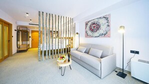 Un soggiorno moderno con un divano, un elemento decorativo a parete, una lampada da terra e un tavolino con una bottiglia e della frutta.